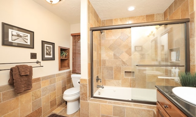 full bathroom with toilet, combined bath / shower with glass door, tile walls, a textured ceiling, and vanity