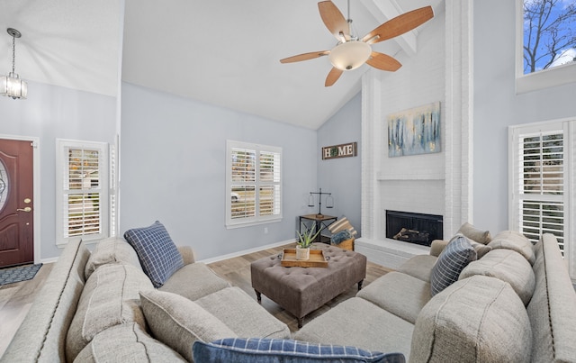 living room featuring high vaulted ceiling, a fireplace, light hardwood / wood-style floors, ceiling fan with notable chandelier, and beamed ceiling