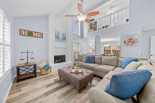 living room with ceiling fan with notable chandelier, high vaulted ceiling, a large fireplace, light hardwood / wood-style floors, and beam ceiling