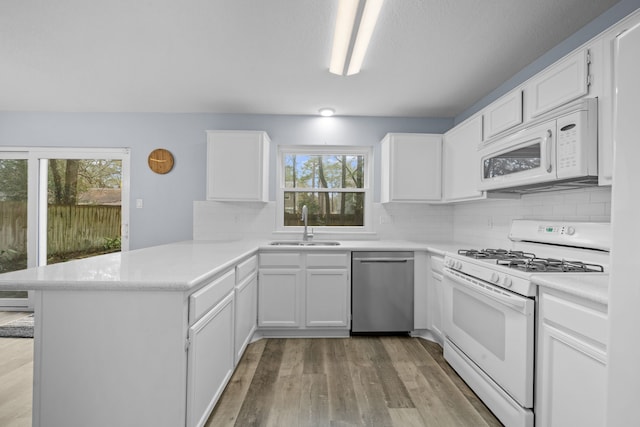 kitchen with white cabinetry, sink, white appliances, and kitchen peninsula