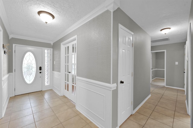 foyer entrance with ornamental molding, a textured ceiling, and light tile patterned floors