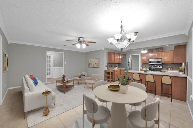 tiled dining area featuring crown molding, ceiling fan with notable chandelier, sink, and a textured ceiling