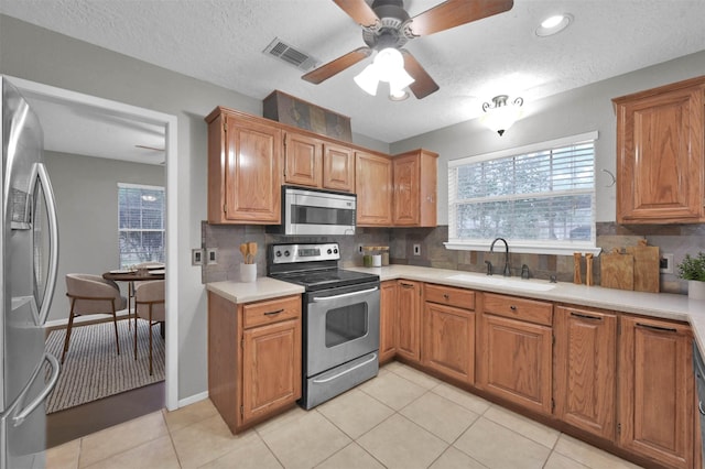 kitchen with appliances with stainless steel finishes, sink, decorative backsplash, light tile patterned floors, and a textured ceiling