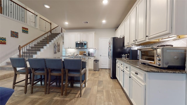 kitchen featuring appliances with stainless steel finishes, tasteful backsplash, white cabinets, dark stone counters, and light wood-type flooring