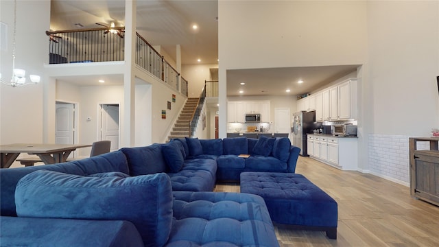 living room with ceiling fan with notable chandelier, light wood-type flooring, and a high ceiling