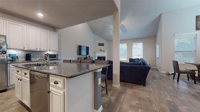 kitchen featuring sink, white cabinetry, vaulted ceiling, appliances with stainless steel finishes, and a kitchen island with sink