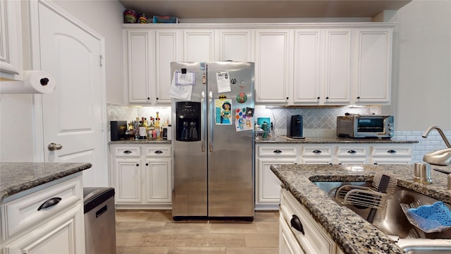 kitchen with white cabinetry, sink, stainless steel fridge, and dark stone countertops