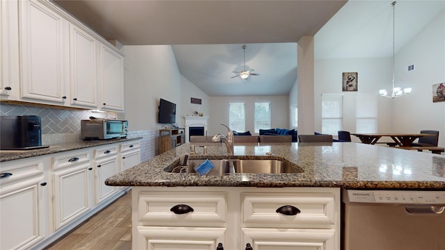 kitchen featuring sink, tasteful backsplash, stainless steel dishwasher, dark stone counters, and a kitchen island with sink