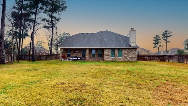 back house at dusk featuring a lawn