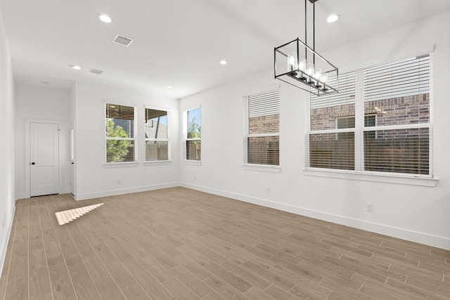 unfurnished room with an inviting chandelier and light hardwood / wood-style flooring