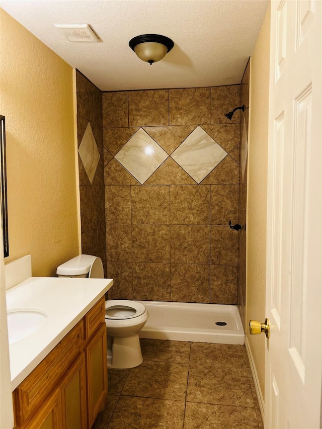 bathroom with vanity, tiled shower, a textured ceiling, and toilet