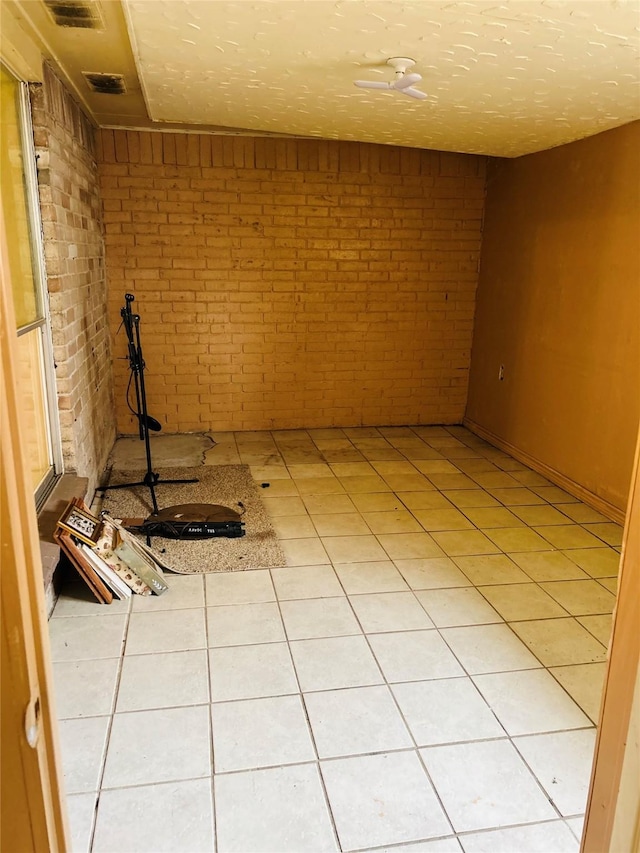 basement with brick wall, tile patterned flooring, and a textured ceiling