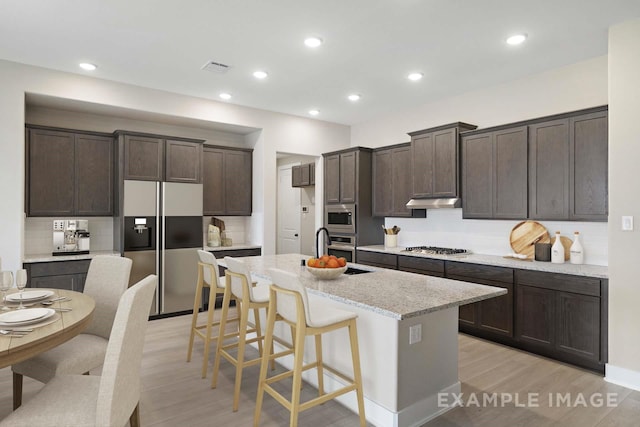 kitchen with built in appliances, dark brown cabinets, a kitchen island with sink, and light wood-style floors