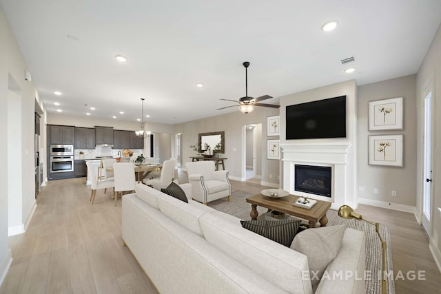 living room with recessed lighting, visible vents, light wood-style flooring, a glass covered fireplace, and baseboards