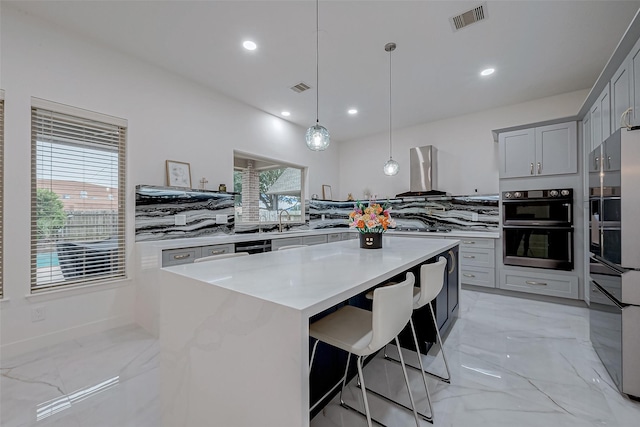 kitchen featuring hanging light fixtures, a wealth of natural light, a center island, and wall chimney exhaust hood