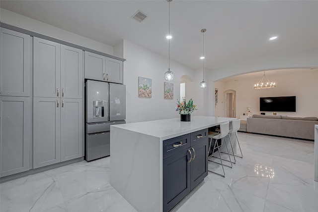 kitchen featuring a breakfast bar, gray cabinetry, decorative light fixtures, stainless steel fridge, and a kitchen island