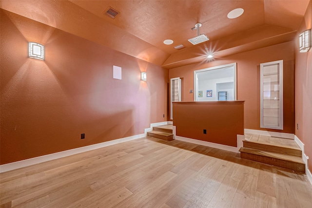 empty room featuring lofted ceiling, light hardwood / wood-style flooring, and a textured ceiling