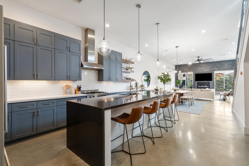 kitchen with a breakfast bar, pendant lighting, tasteful backsplash, an island with sink, and wall chimney exhaust hood