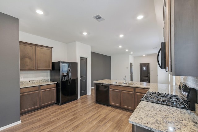 kitchen featuring light stone counters, sink, light hardwood / wood-style flooring, and black appliances