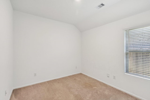 empty room featuring vaulted ceiling, a healthy amount of sunlight, and light colored carpet