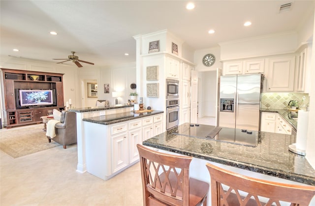 kitchen with a breakfast bar area, dark stone countertops, kitchen peninsula, stainless steel appliances, and white cabinets