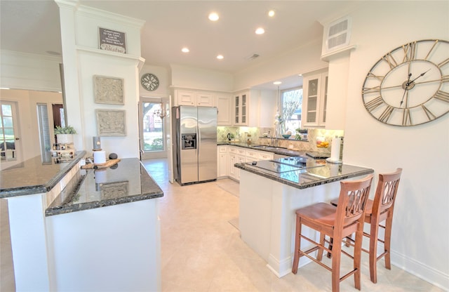 kitchen with dark stone countertops, a kitchen breakfast bar, white cabinets, stainless steel fridge with ice dispenser, and kitchen peninsula