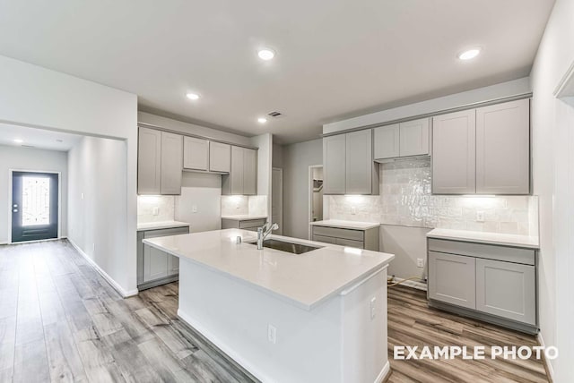 kitchen featuring light wood-type flooring, a kitchen island with sink, a sink, and gray cabinetry