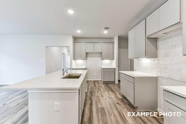 kitchen with visible vents, decorative backsplash, light wood-style flooring, gray cabinets, and a sink