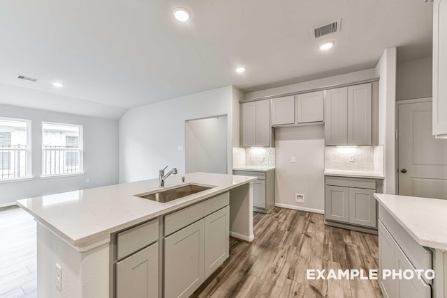 kitchen with a kitchen island with sink, wood finished floors, a sink, visible vents, and decorative backsplash