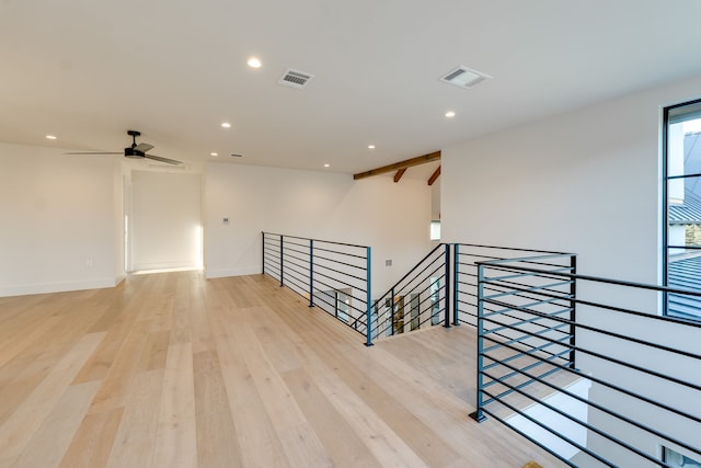 empty room with ceiling fan, beam ceiling, and light wood-type flooring