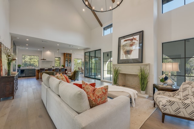 living room with beam ceiling, a notable chandelier, a towering ceiling, and hardwood / wood-style flooring