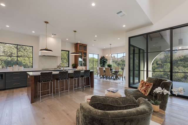 kitchen with pendant lighting, backsplash, a center island with sink, light hardwood / wood-style floors, and a kitchen bar