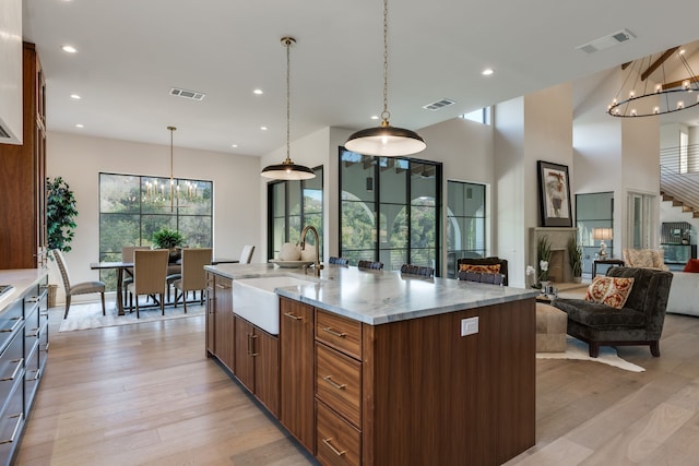 kitchen with sink, a kitchen island with sink, hanging light fixtures, light stone counters, and a notable chandelier