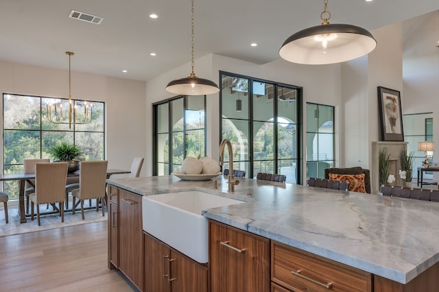 kitchen featuring an island with sink, light stone countertops, sink, and decorative light fixtures