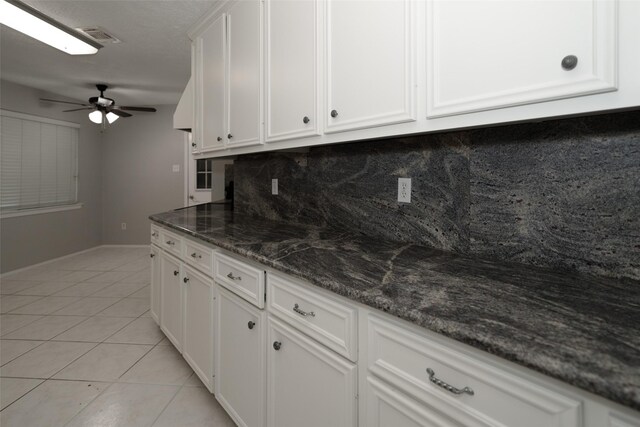 kitchen featuring white cabinetry, backsplash, dark stone counters, light tile patterned floors, and ceiling fan