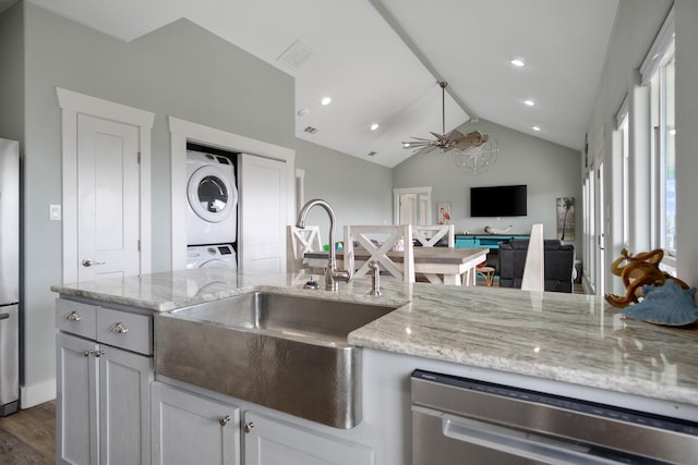 kitchen featuring a sink, appliances with stainless steel finishes, stacked washer / drying machine, light stone countertops, and vaulted ceiling