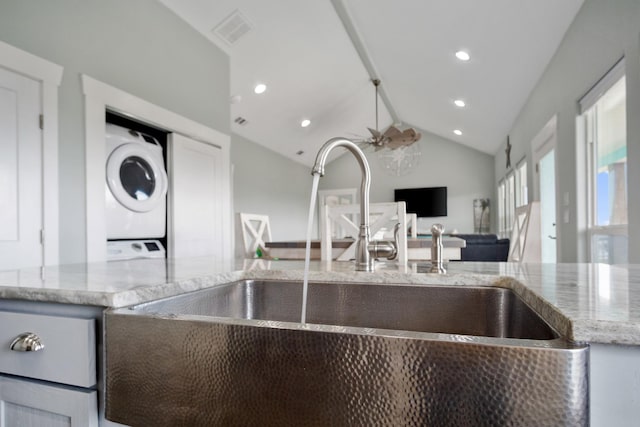 kitchen featuring visible vents, a sink, stacked washer / dryer, lofted ceiling, and light stone countertops