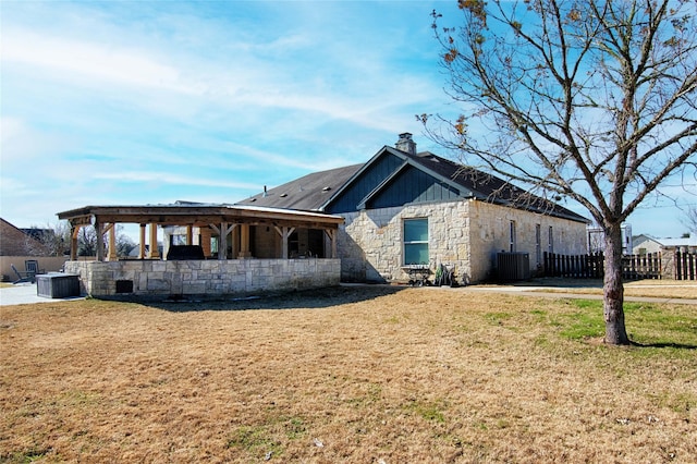 exterior space featuring central AC unit, stone siding, a lawn, a chimney, and fence
