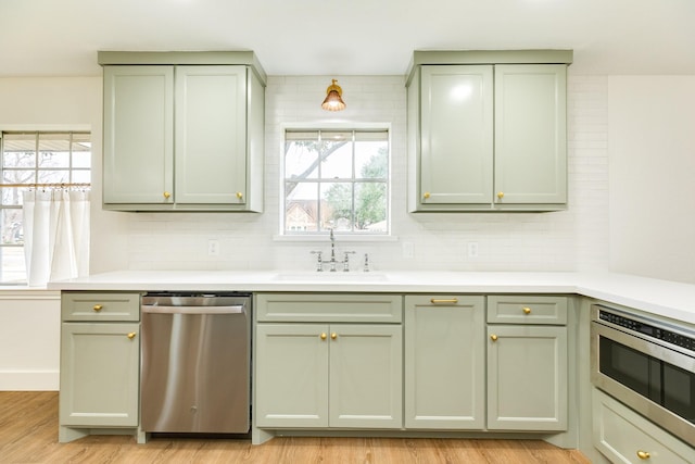 kitchen featuring appliances with stainless steel finishes, sink, decorative backsplash, and light wood-type flooring