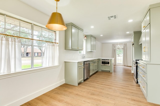 kitchen with hanging light fixtures, appliances with stainless steel finishes, backsplash, and light wood-type flooring