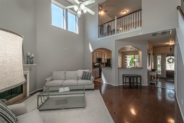 living room with a high ceiling, a tile fireplace, dark hardwood / wood-style floors, and ceiling fan