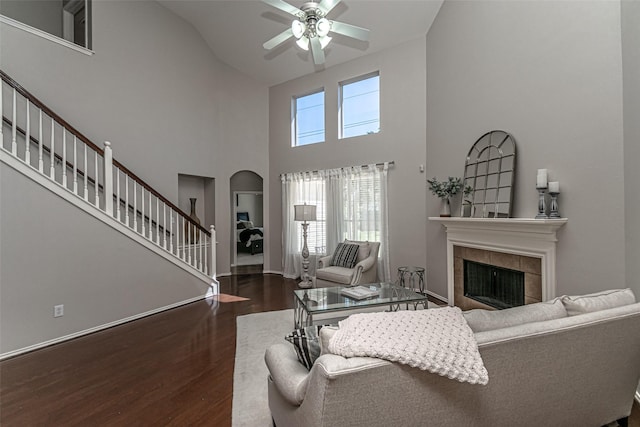 living room featuring a high ceiling, a tile fireplace, dark hardwood / wood-style floors, and ceiling fan