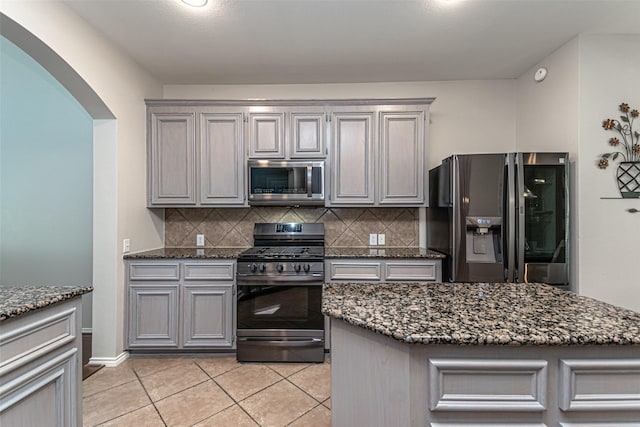 kitchen with gray cabinets, appliances with stainless steel finishes, tasteful backsplash, light tile patterned flooring, and dark stone counters