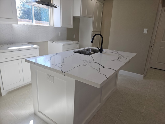 kitchen featuring a kitchen island with sink, sink, light stone counters, and exhaust hood