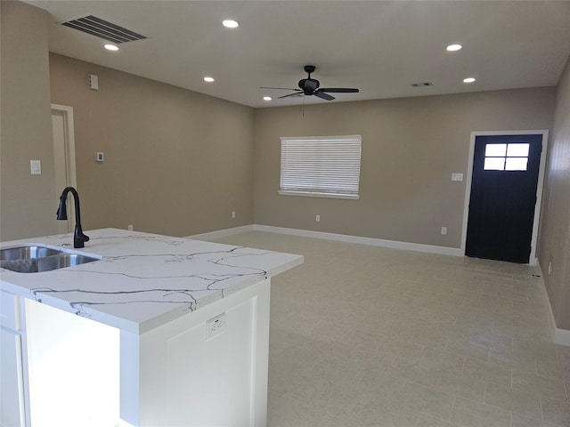 kitchen featuring sink, white cabinetry, an island with sink, ceiling fan, and light stone countertops