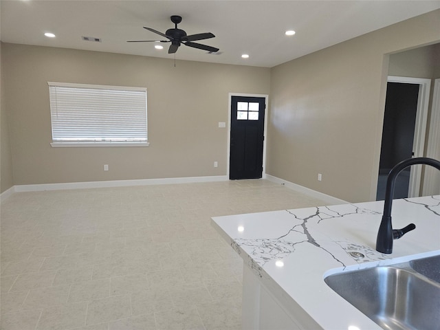 kitchen featuring light stone counters, ceiling fan, and sink