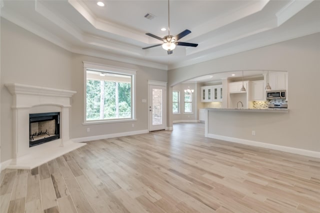 unfurnished living room featuring sink, light hardwood / wood-style flooring, ceiling fan, ornamental molding, and a raised ceiling