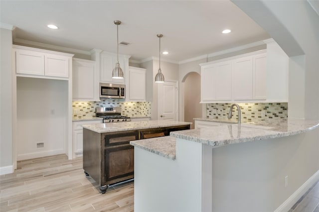 kitchen with light stone counters, kitchen peninsula, pendant lighting, stainless steel appliances, and white cabinets