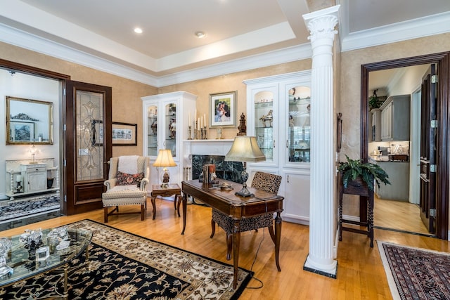 living area with a tray ceiling, light hardwood / wood-style floors, and ornate columns