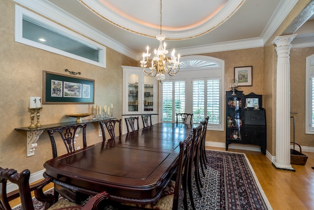 dining space featuring crown molding, a chandelier, decorative columns, and light hardwood / wood-style flooring